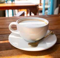 Thai hot tea with foam in white cup on saucer on table close-up