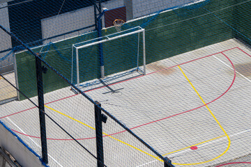 Perspective top view of school multi-sport court with painted concrete floor surrounded by fencing and protective upper screen

