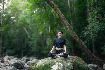 A woman meditating with a waterfall surrounded by nature, looking relaxed and stress-relieving