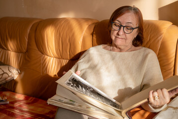 Senior lady looking at old photographs in the album, remembering her past and her baby, family. 