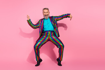Eccentric elderly man in vibrant suit dancing on pink background for celebration or party