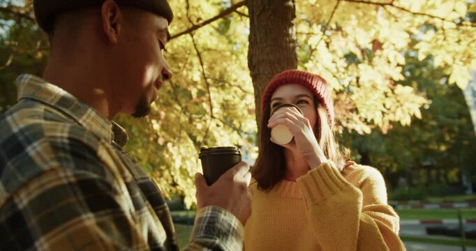 Cheerful brunette girl drinks coffee and chats with her boyfriend during a date in a sunny autumn park
