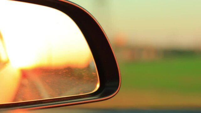 The sun is reflected in the mirror, evening road. View in the side rear view mirror of a red car driving along the highway
