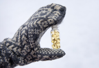 Vitamin D keeps you healthy while lack of sun in Nordic countries in the winter. Yellow soft shell D-vitamin capsules against white snow in glass jar.