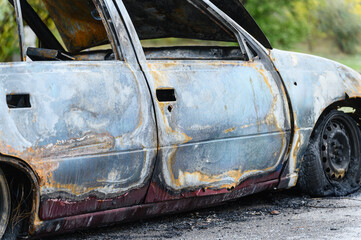 Burned car wreck abandoned on roadside in nature