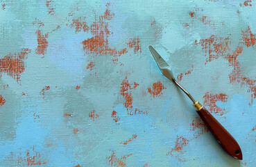 Palette knife on a painting canvas. The artist's metal tool with a wooden brown handle, with blue paint, lies on a canvas with an abstract acrylic painting.