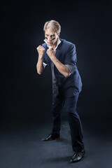 In a dimly lit studio, a man in a navy suit adopts a boxing stance, showcasing strength and...