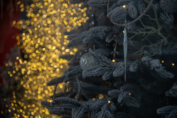 A snowy evergreen tree adorned with shimmering ornaments and delicate icicles glows against a backdrop of blurred golden lights, creating a warm winter atmosphere.