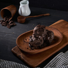 Indulge in rich chocolate ice cream adorned with crushed cookie pieces, elegantly presented in a wooden bowl on a rustic table