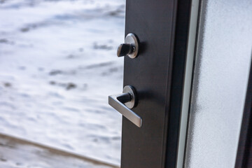 a close-up of a black door with a silver door handle. The door is slightly ajar, revealing a snowy scene outside. The door handle is modern and sleek, with a simple design.