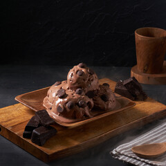Delicious chocolate ice cream topped with chocolate chips and dark chocolate pieces is beautifully arranged on a wooden platter