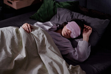 High angle shot of adult woman lying on her side in bed, she resting after night shift in dimly lit...