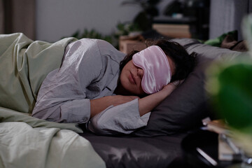 Medium close up of woman in lila pajamas and silk sleep mask on eyes sleeping with hands under head