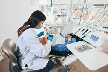 Naklejka premium Female doctor in gloves and mask carefully cleaning teeth of elderly woman in dental chair, working in calm and well-organized clinic. Concept of healthcare and pensioners, medicine.