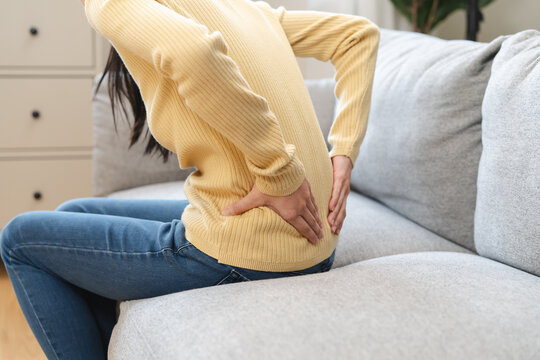 Close-up woman massaging her lower back has back pain because of sitting posture during work in office.