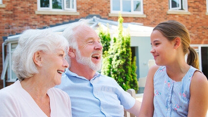 Granddaughter Sitting On Bench With Grandparents During Visit To Retirement Home