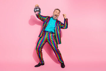 Elderly man wearing rainbow suit with disco ball and pink background showing energy and charm