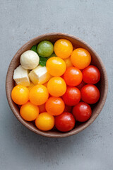 A colorful assortment of melon balls in a bowl, featuring various shades of yellow, red, orange, and green, alongside cubes of cheese for a delightful snack.