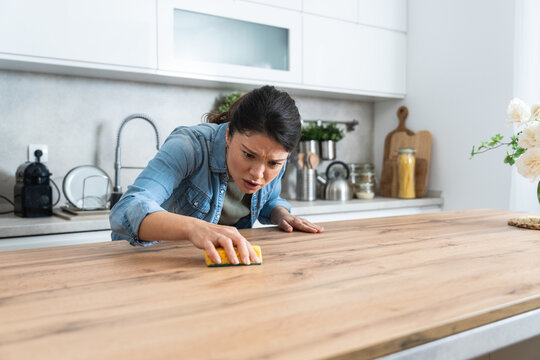 Young woman suffers from depression after a breakup or divorce and from obsessive compulsive disorder OCD cleans kitchen cook top to calm her nerves. Serious stressed female rubbing the home