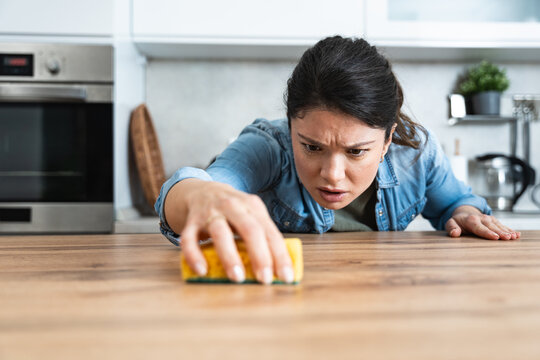 Young woman suffers from depression after a breakup or divorce and from obsessive compulsive disorder OCD cleans kitchen cook top to calm her nerves. Serious stressed female rubbing the home