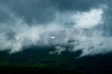 Low hanging, dark clouds obscure a mountain top with patches of snow, creating a dramatic and moody atmosphere, hinting at an impending storm