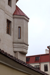 
A corner of an old building with a protruding tower and a red roof that contrasts with the gray wall of the house.