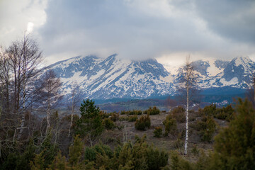 Stunning snow capped mountain peaks rising majestically above a lush green valley create a breathtaking landscape, all under a dramatic, cloudy sky that enhances the serene atmosphere