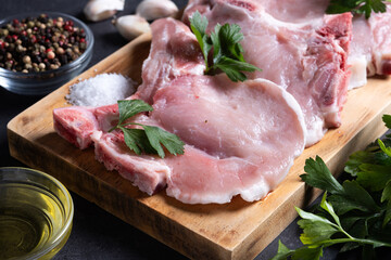 Fresh uncooked pork chops on cutting board and black stone background