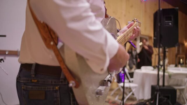 Close up of hands and fingers strumming as country player plays classic wooden acoustic guitar at small event space and wedding reception at bar and restaurant in close up and no faces with blur