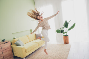 Joyful young woman with blond hair enjoying a relaxing weekend at home in a stylish living room,...