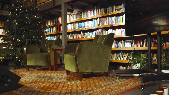Stage for reading or podcasts in a vintage and retro library with two couches on the stage with studio monitors and retro carpet. Bookshelves with books are in the background with Christmas tree also.