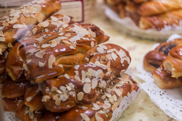 Freshly baked pastries stacked high, adorned with almond slices, draw attention in a cozy bakery. The warm brown tones and inviting aroma create a delightful atmosphere for visitors.