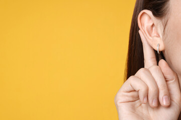 Woman showing hand to ear gesture on orange background, closeup. Space for text