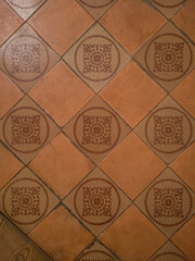 Brown ceramic tile with a floral pattern, laid in a diagonal pattern. Top view.