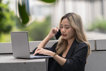Professional woman working on a laptop outdoors, exuding confidence and focus while multitasking in...