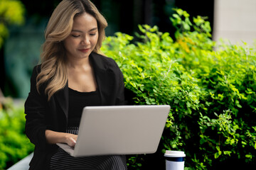 Young professional using her laptop while seated in a green urban space. A portrayal of a modern career lifestyle, highlighting technology, focus, and outdoor productivity.