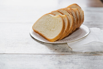 Sliced loaf neatly arranged on a white disposable plate. Rye bread slices on a plastic plate resting on a wooden surface; simple baking; concept - economy and life
