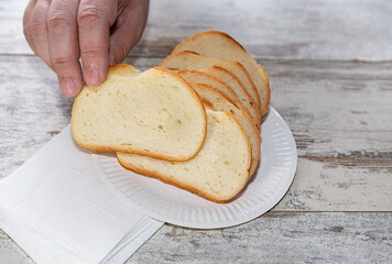 a hand reaching for a piece of bread from a plate of sliced bread on a wooden table