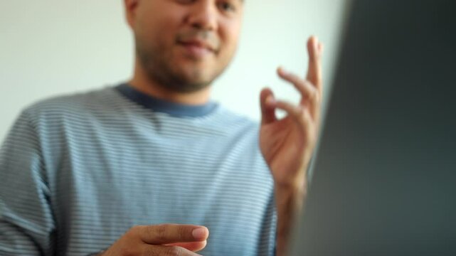 Close up of fingers and hands showing sign language for communication  by video call using laptop at home, a man with hearing disability showing hand gestures to mute impaired people via online.

