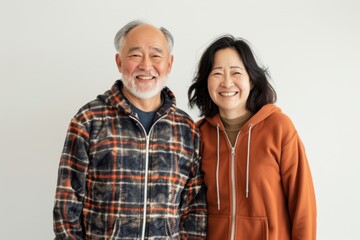 Portrait of a joyful asian couple in their 60s wearing a zip-up fleece hoodie in white background