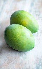 Obraz premium Two green mangoes on a light wooden table, top view, stock photo, close-up. 