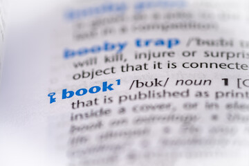 Book word in a dictionary. Selective focus, close up.