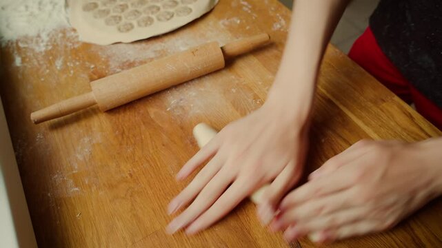 Teenager rolling dough with hands forming smooth cylindrical shape. Table sprinkled with flour for easy handling. Rolling pin resting nearby ready for next step. Preparing dumpling ingredients