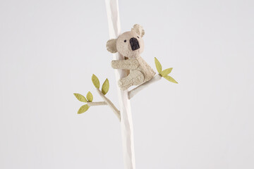 Handmade koala figurine climbing a tree branch with green leaves on a white background. Minimalist paper craft animal sculpture. Design for greeting card, invitation, poster, and decoration