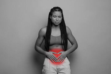 Gastrointestinal disease, period cramps concept. Unhappy african american young woman in pain touching her belly sore zone lightened in red, monochrome studio photo, copy space. High quality photo