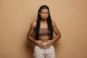 African woman touching aching abdomen having painful stomachache standing over beige studio...