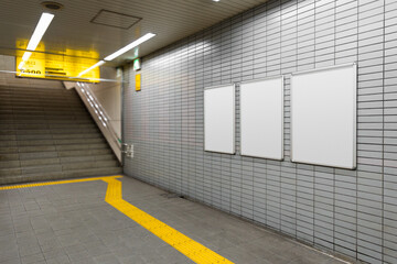 Three blank billboard poster on a subway station wall beside exit stairs. Space for text for...