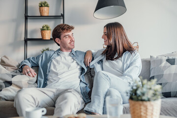 Young happy couple having fun talking laughing relaxing at home on couch, boyfriend embracing...