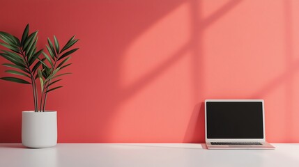 Fototapeta premium A minimalistic workspace featuring a laptop and a potted plant on a vibrant coral wall.