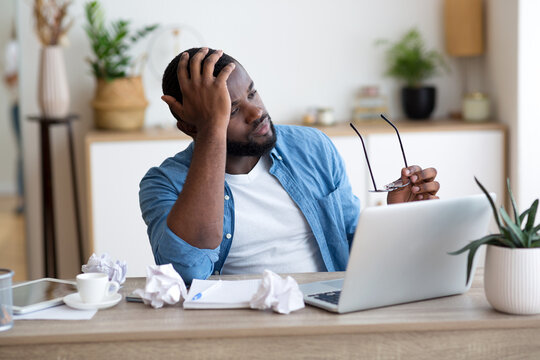 Stressed african Male Entrepreneur Having Problems At Work. Depressed African American Man Sitting Upset At Desk With Laptop In Office And Touching Head In Despair, Closeup Shot With Free Space. High